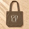The Clubhouse Tote flat lay, a walnut canvas golf tote with GOLF wordmark print and golf accessories by Fore & Femme