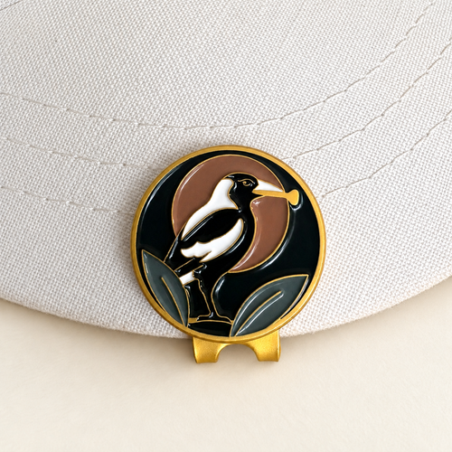 The Course Thief magpie golf ball marker by Fore & Femme clipped to a cream linen cap