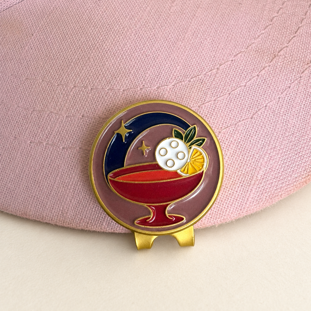 Last Round cocktail golf ball marker by Fore & Femme clipped to a pink linen cap