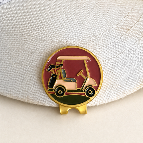 The Shortcut golf cart ball marker by Fore & Femme clipped to a cream linen cap
