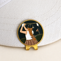 The Follow Through golfer ball marker by Fore & Femme clipped to a cream linen cap