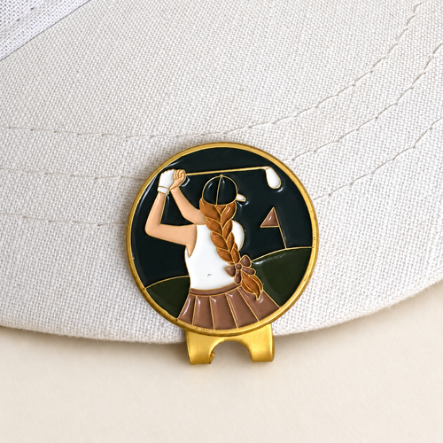 The Follow Through golfer ball marker by Fore & Femme clipped to a cream linen cap