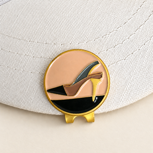 The Tee Heel golf ball marker by Fore & Femme clipped to a cream linen cap